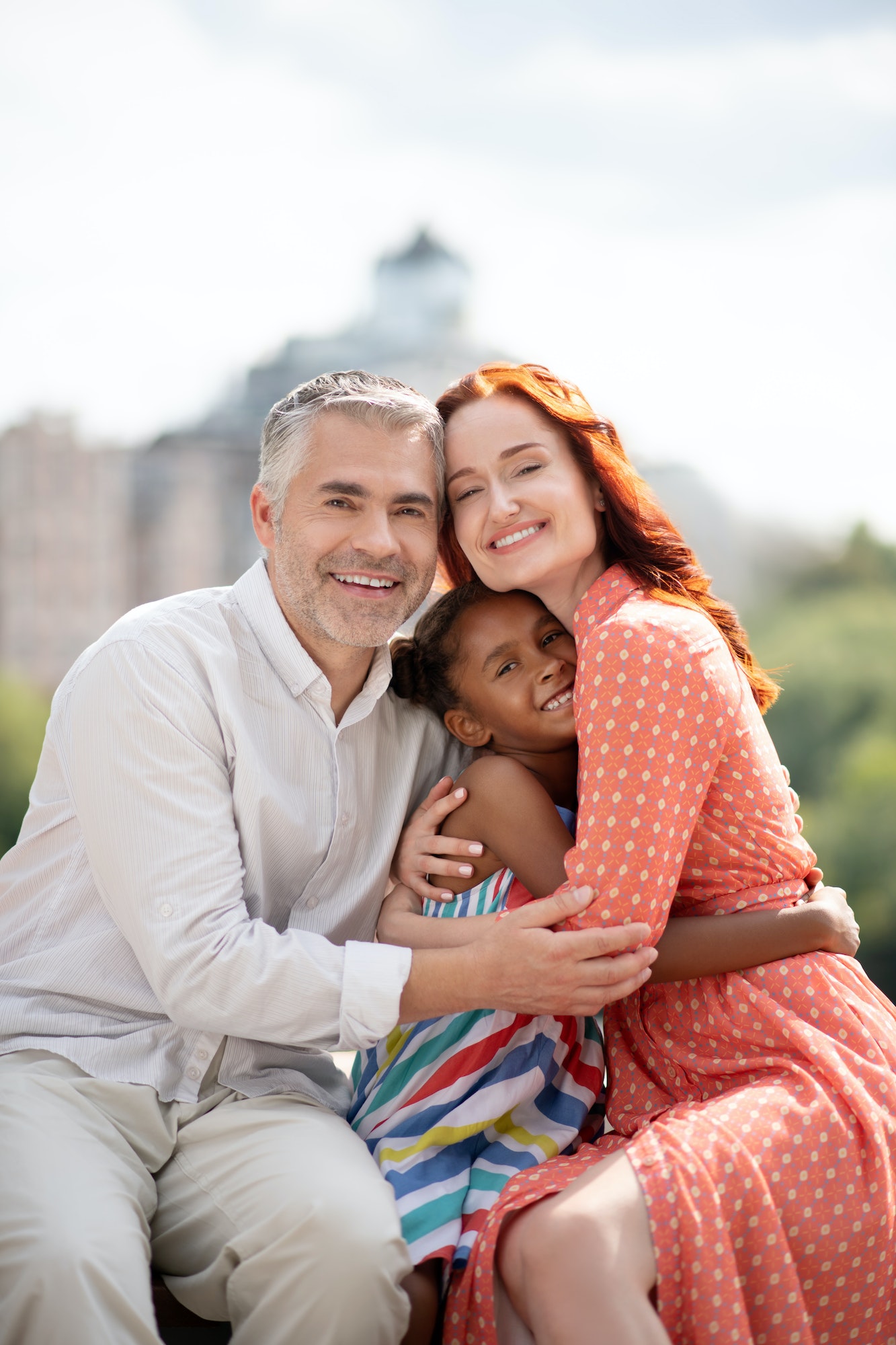 Foster mother and father hugging their cute happy daughter